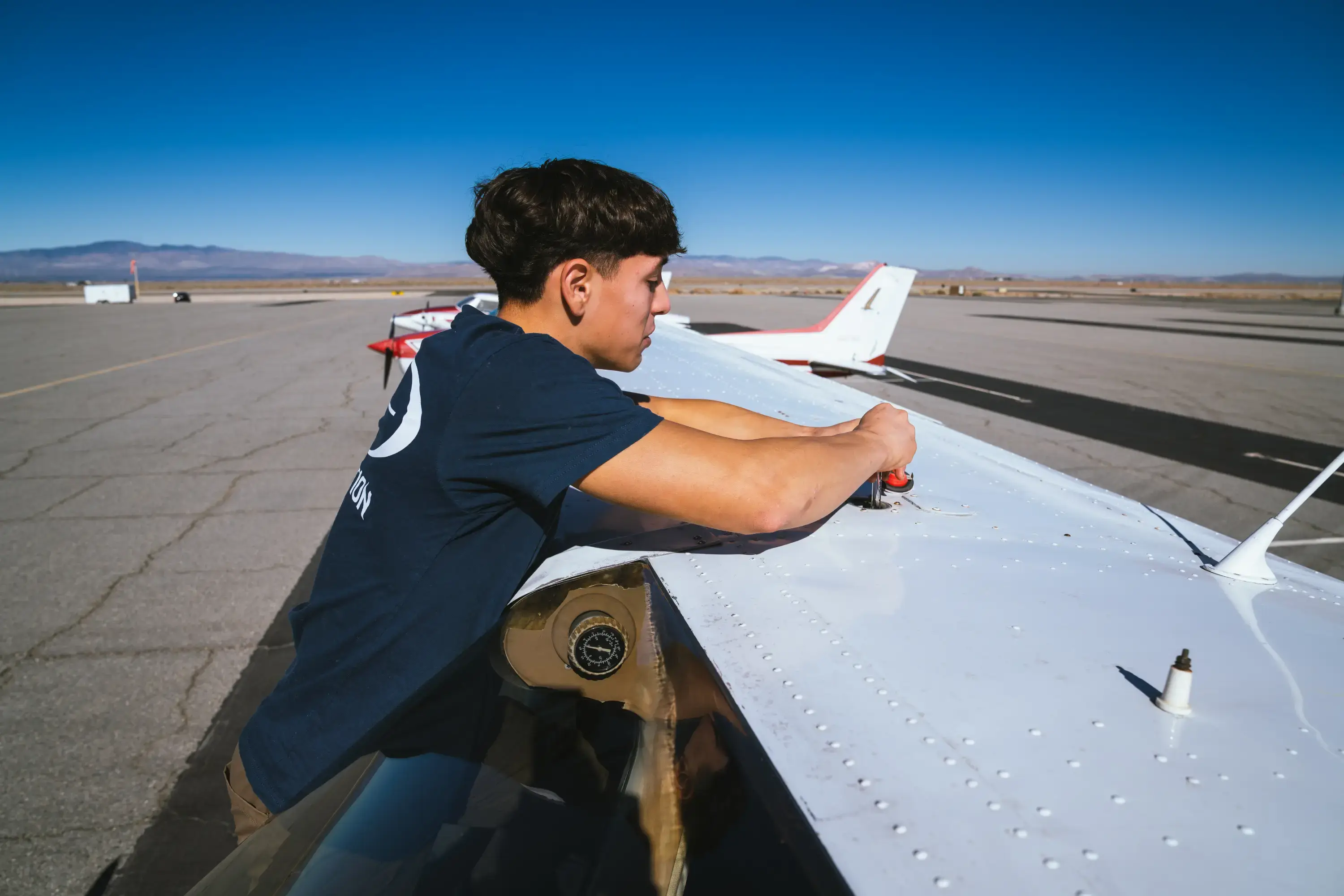 Student checking the fuel cap on the wing of a Cessna during a preflight at Fox Field